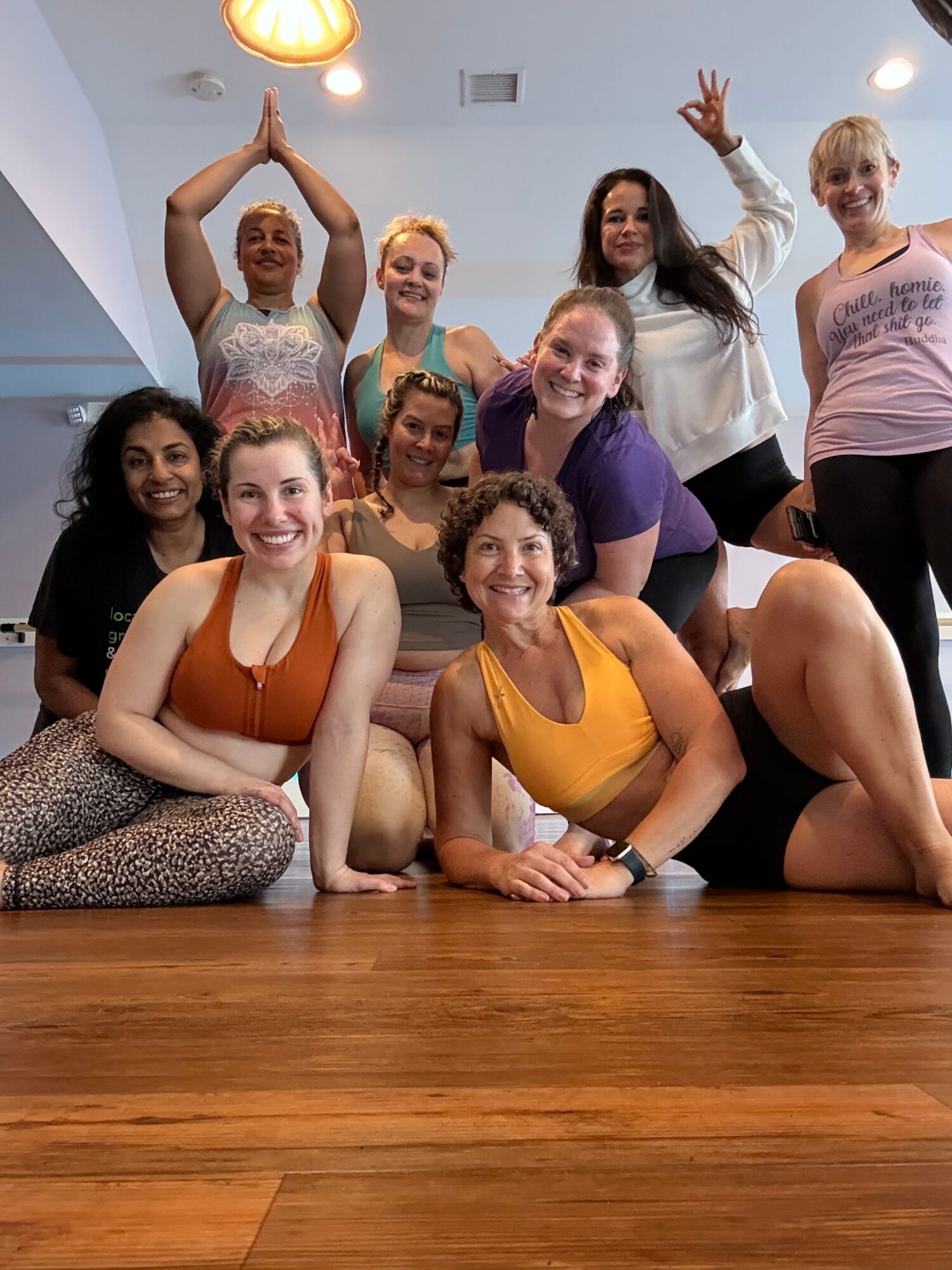 Group of women sitting and lying on a wooden floor, smiling and posing for a photo indoors.