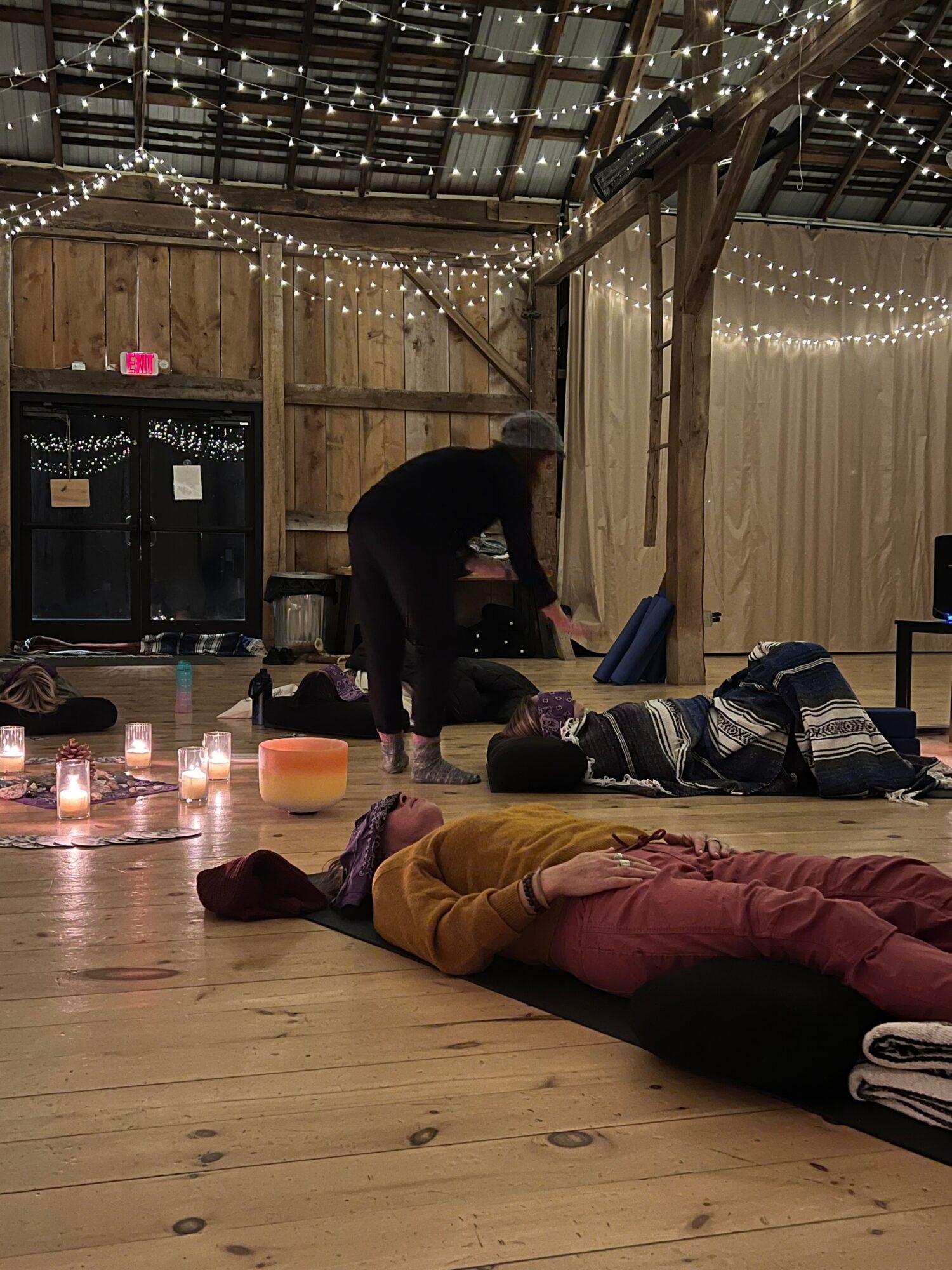 People sitting and lying on the floor in a cozy, decorated indoor space with string lights and wooden walls.