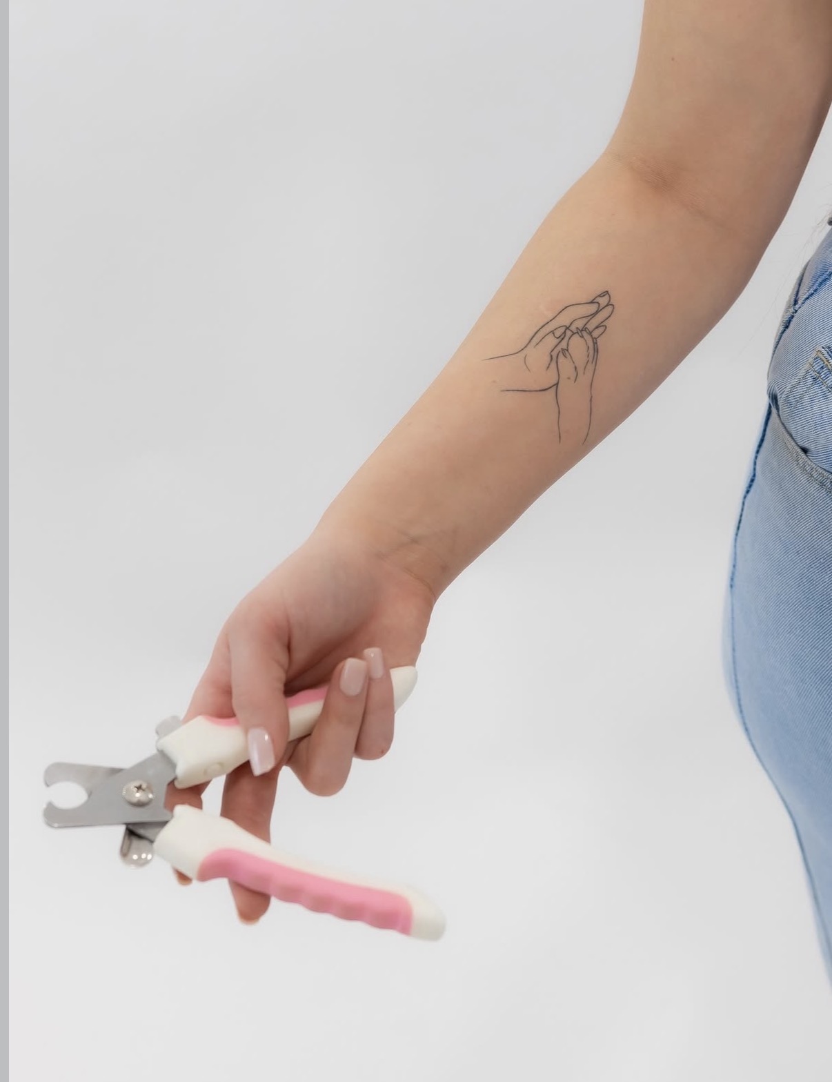 Person's arm with a tattoo of a hand holding a flower, holding a nail clipper, against a plain background.