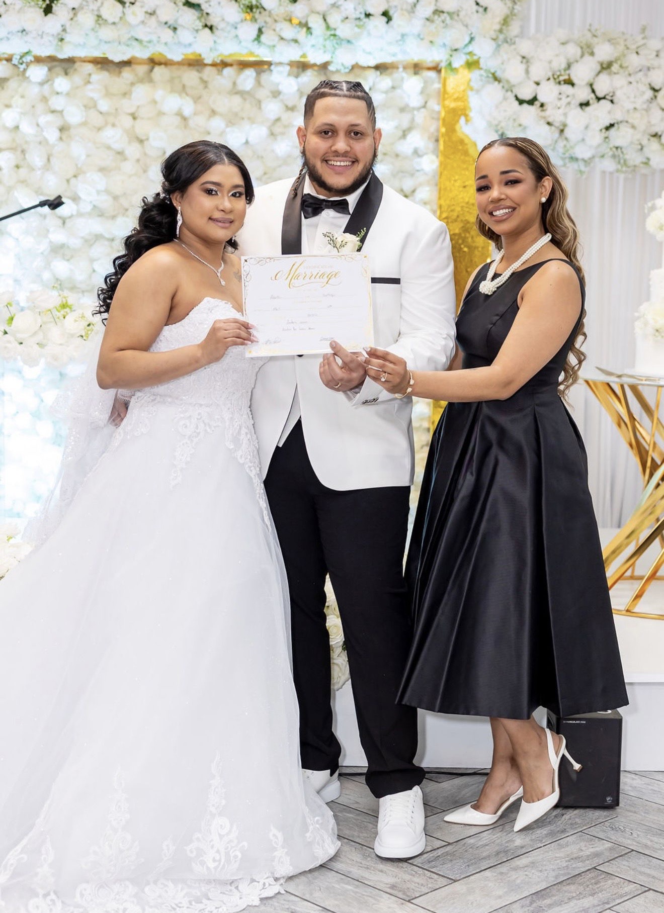 A couple in formal attire hold a certificate with a woman in a black dress beside them.