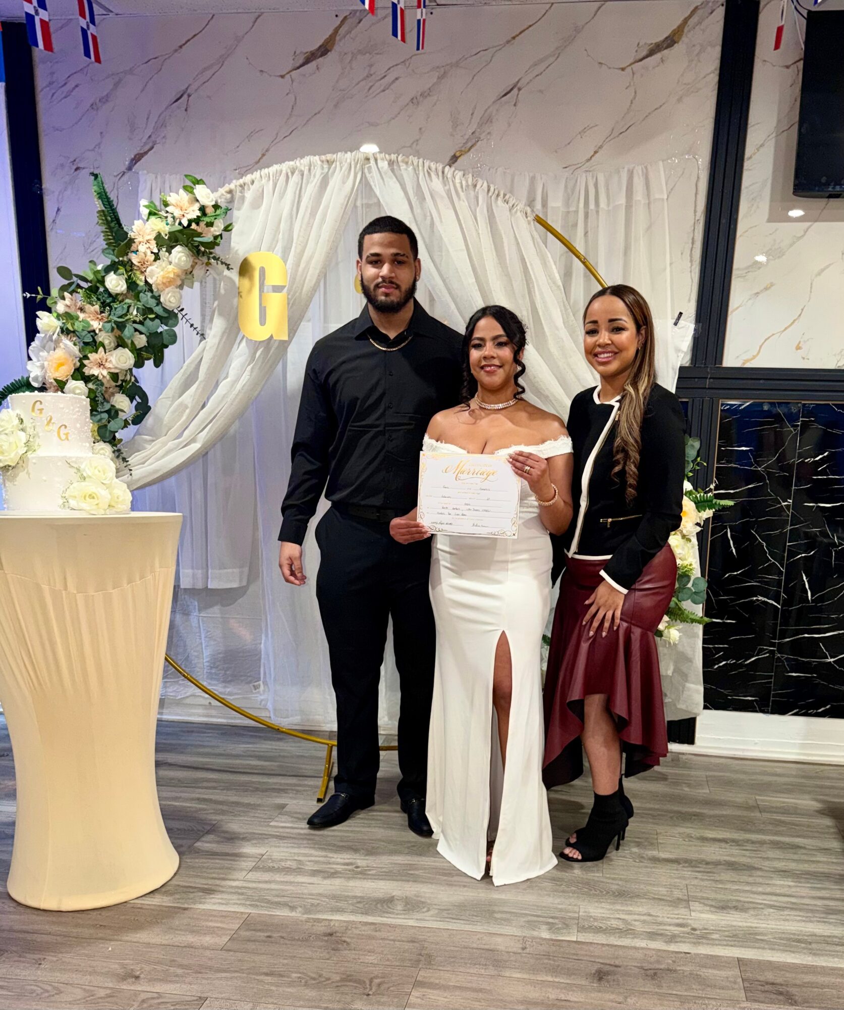 Three people pose together beside a flower-decorated table and a draped backdrop.