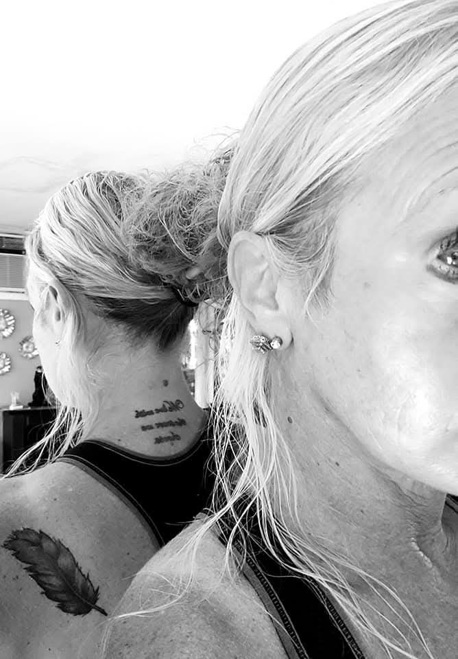 Black-and-white close-up of two people, one facing away with a neck tattoo and shoulder tattoo, and one partially visible in profile.