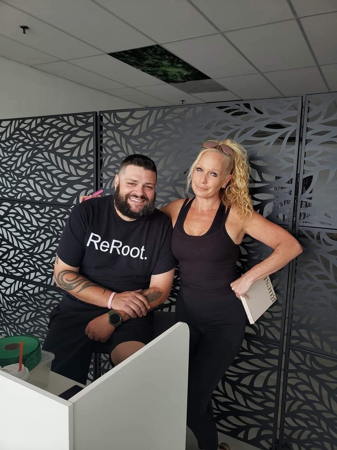 Two adults pose beside a cubicle partition in an office with patterned screens.