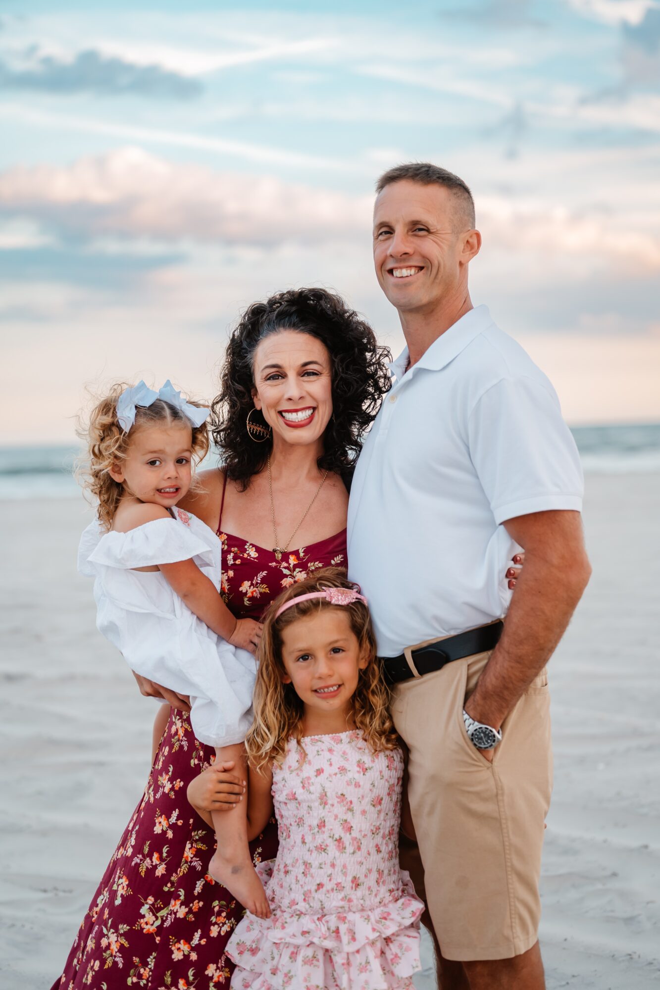 Two adults and two children pose together on a beach beneath a cloudy sky.