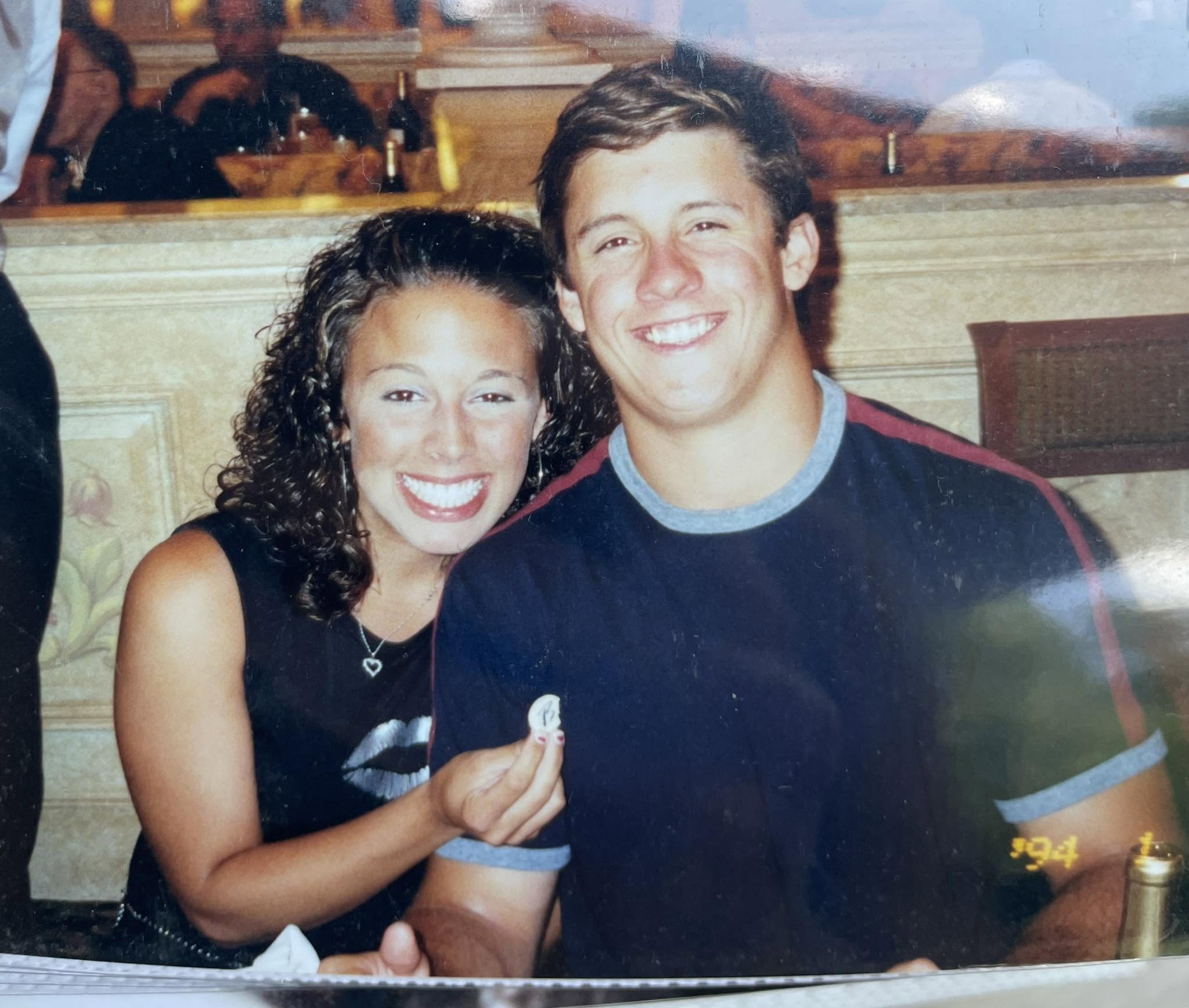 Two people pose together indoors, smiling at the camera.