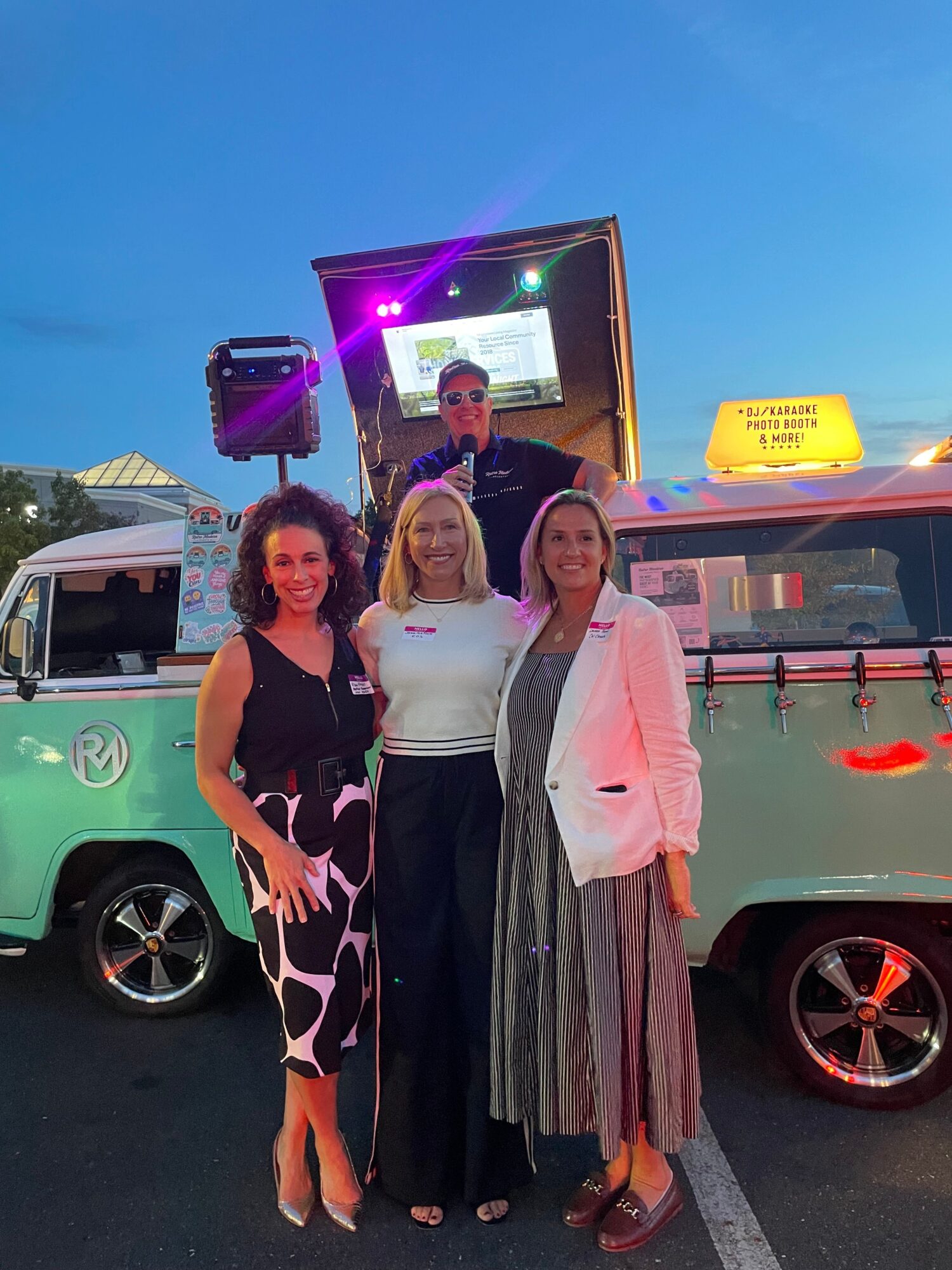 Four people pose beside parked cars at an indoor event.