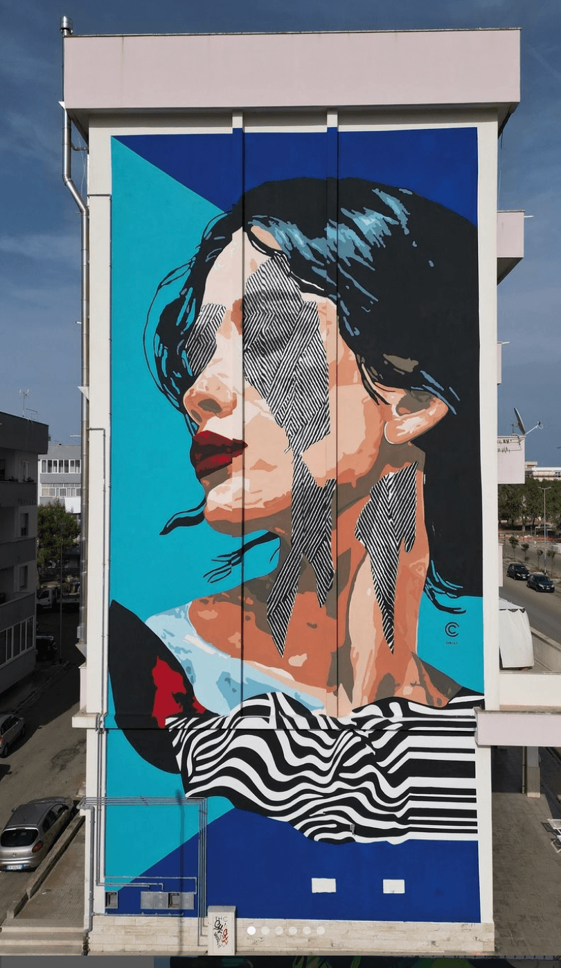 Large mural of a person’s profile with dark hair, a striped shirt, and a turquoise background on a building.