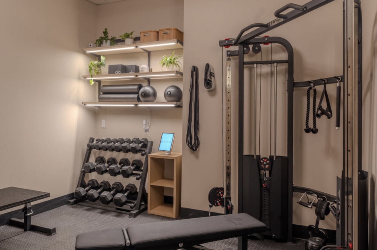 A home gym with a weight rack, dumbbells, a cable machine, shelves, and a workout bench.