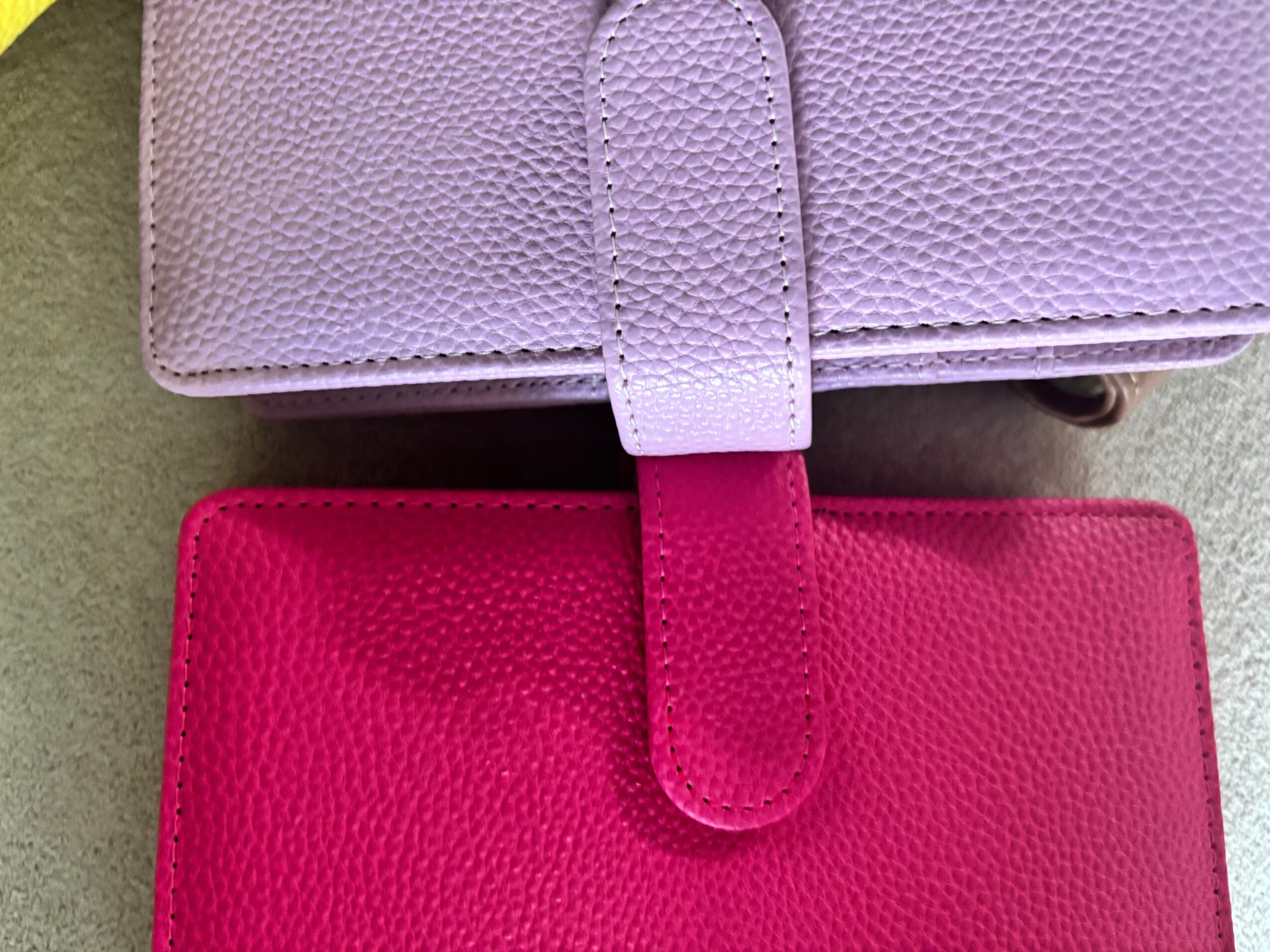 Two textured wallets, one pale lavender and one bright pink, lie on a surface.