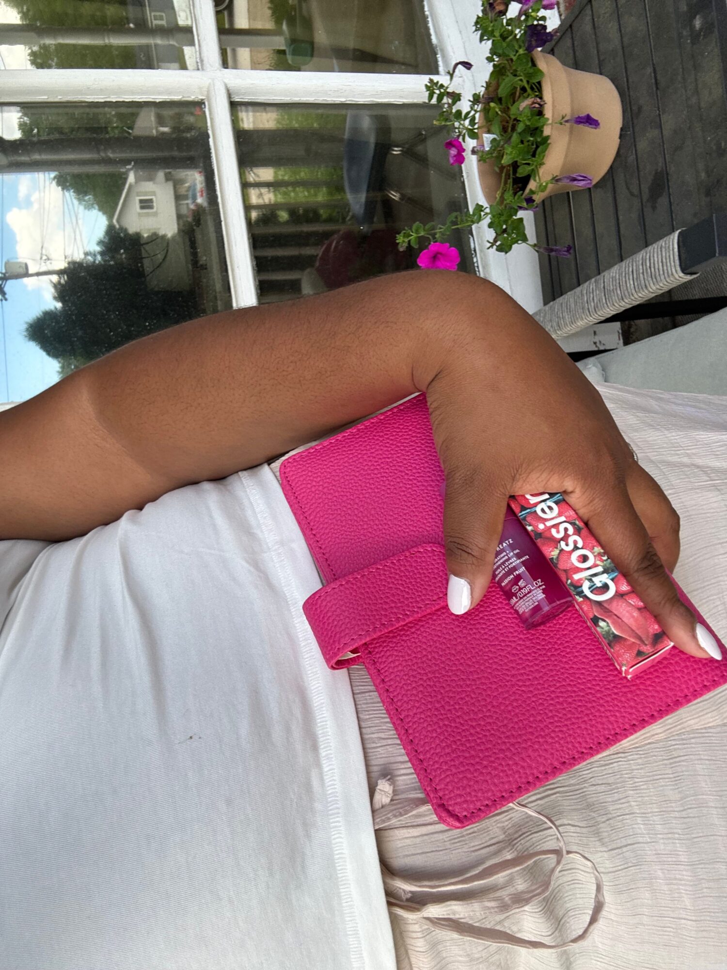 A hand holding a bright pink wallet and a small cosmetic tube beside a white shirt.