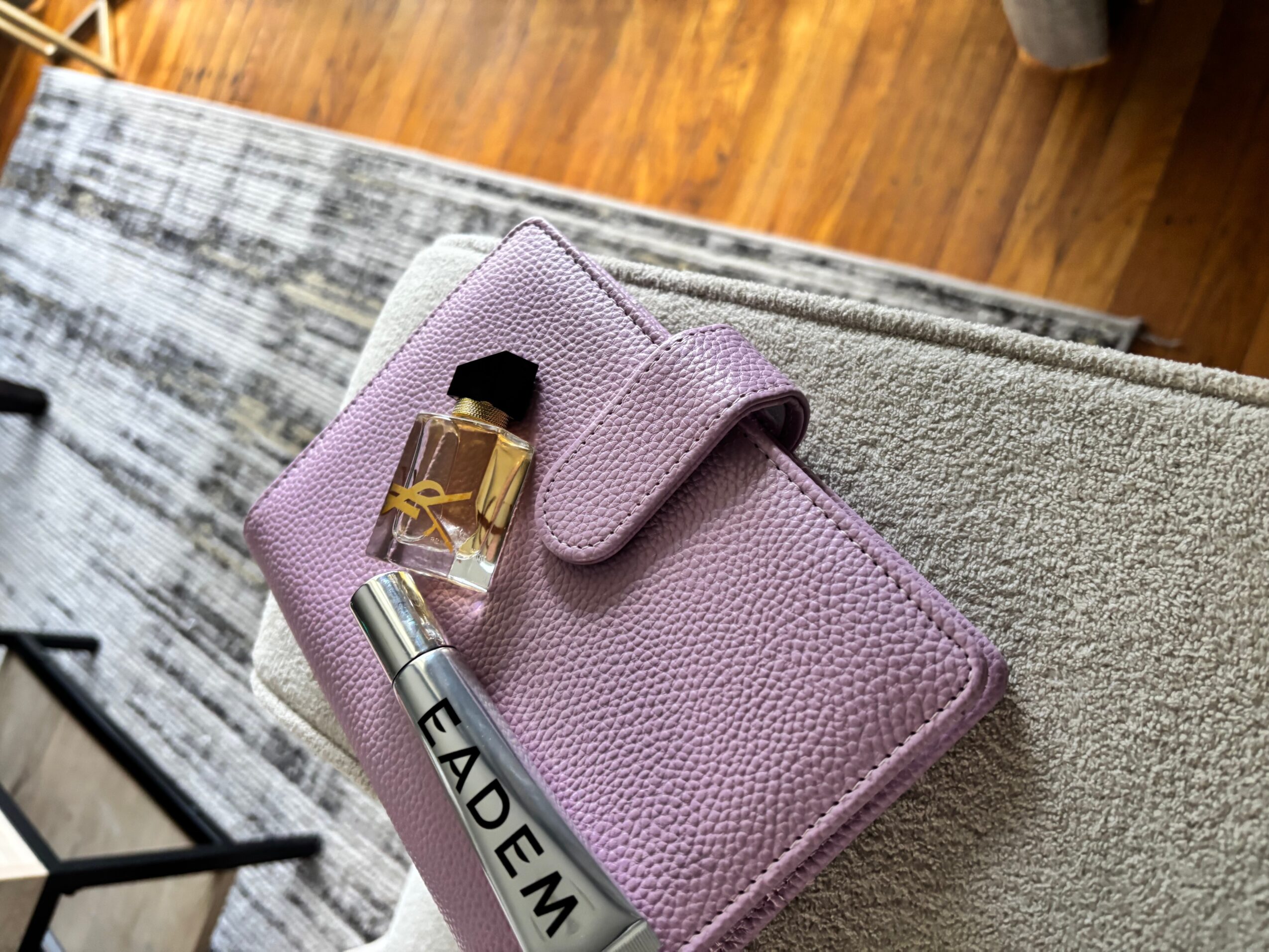 Pink textured wallet with a perfume bottle and silver tube resting on a rug.