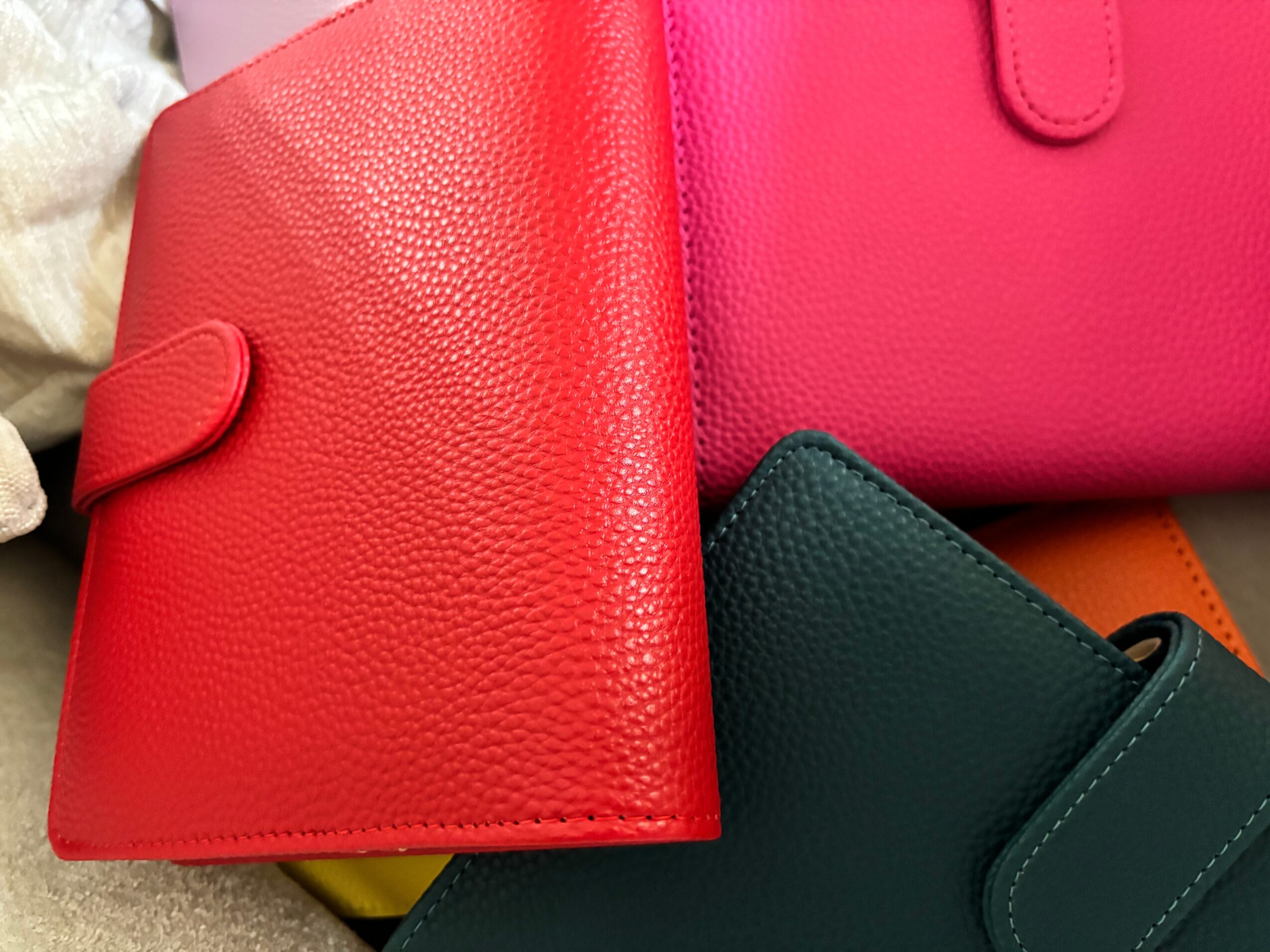 Several colorful textured wallets or small bags overlap on a light surface.