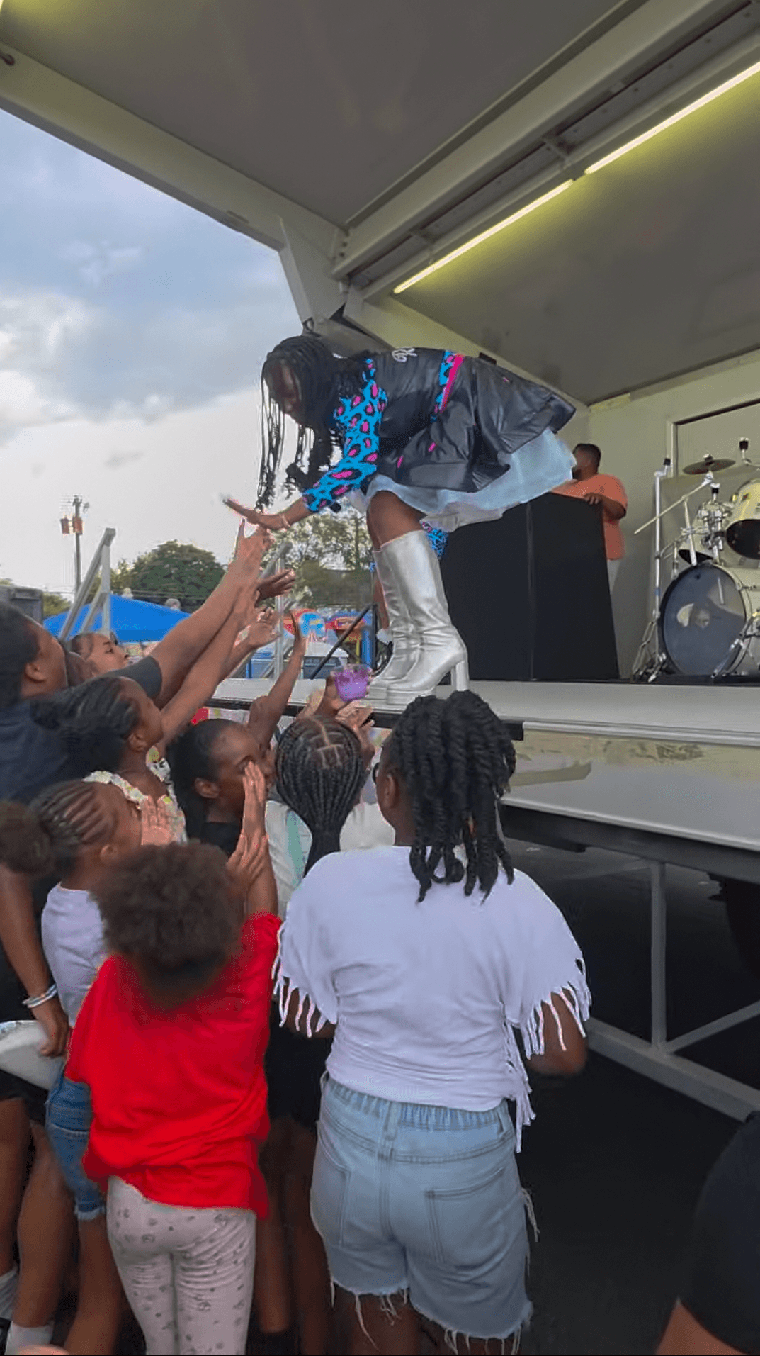 A performer leans toward a crowd reaching up beside an outdoor stage.