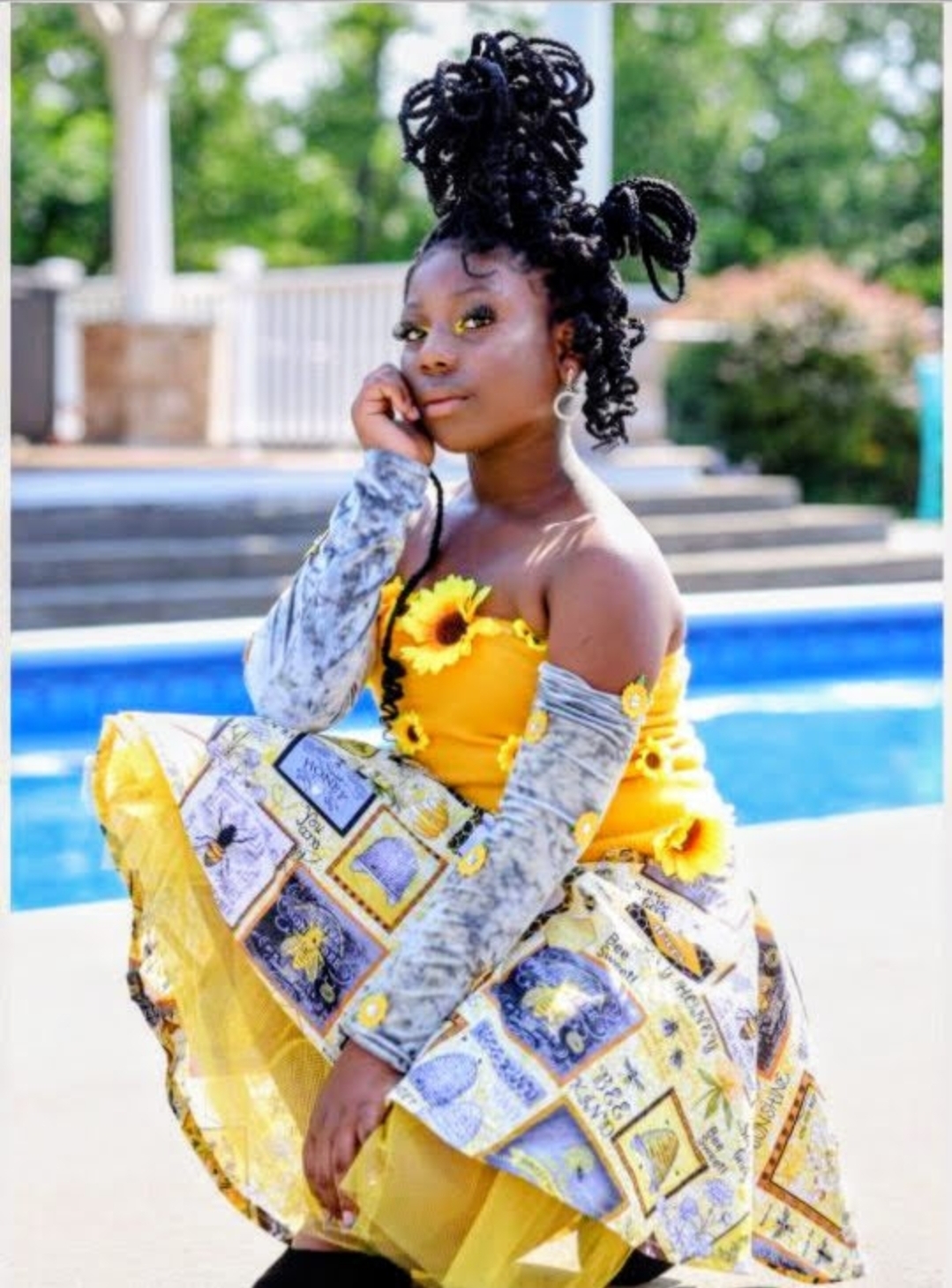 Person in a yellow dress with patterned fabric, seated beside a swimming pool.