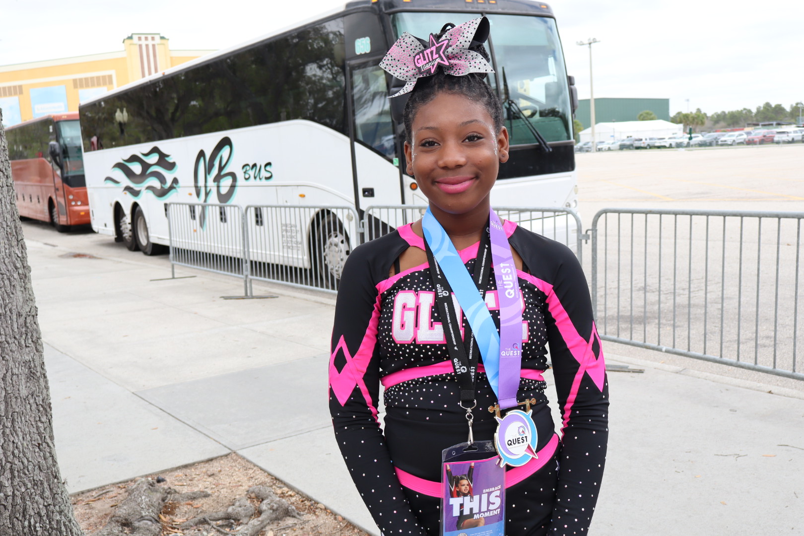 A person in a black and pink outfit with medals stands in front of a parked bus.