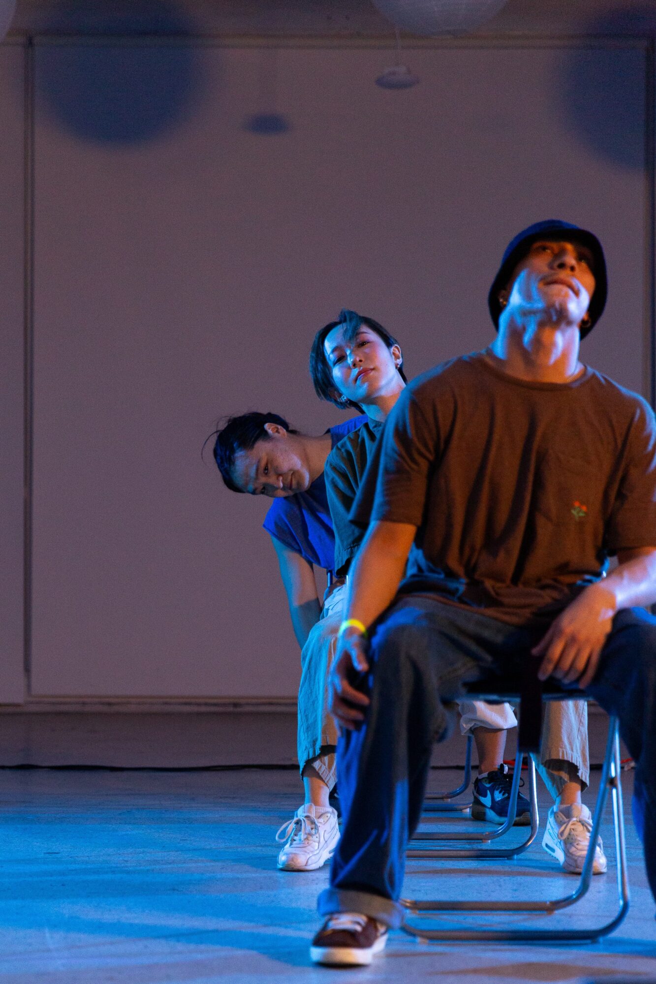 Three people pose in a staggered line on a blue-lit stage, with one seated in front.