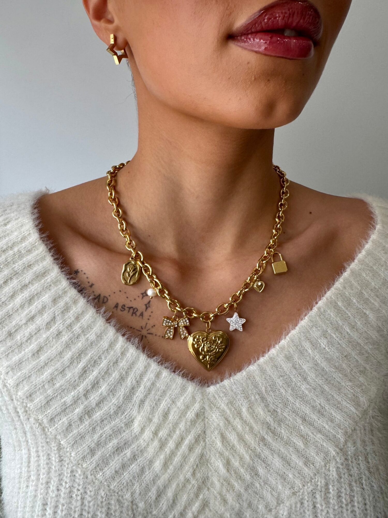 Close-up of a person wearing a white sweater, gold chain necklace with charms, and gold earrings.