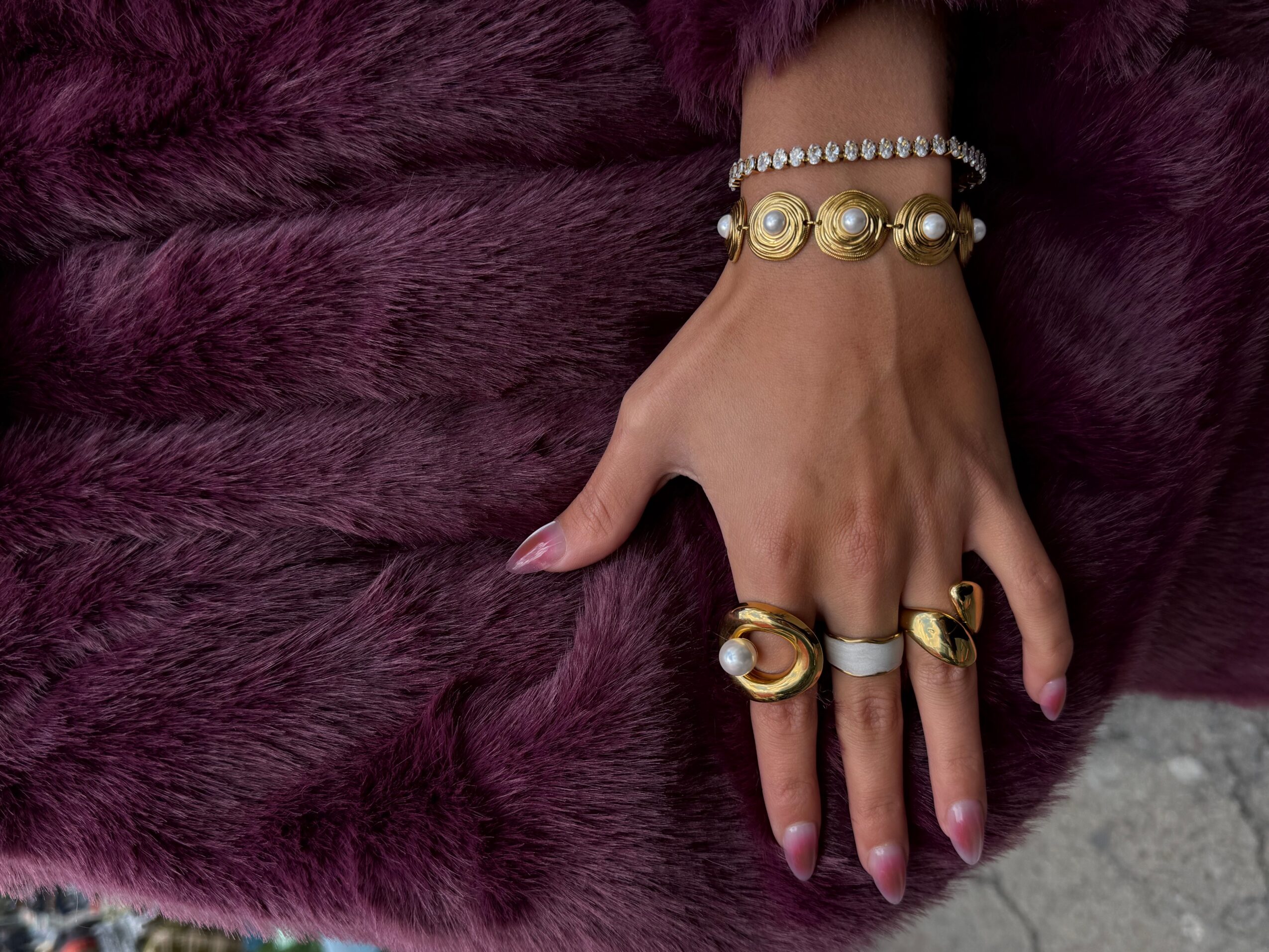 A hand wearing several rings and bracelets rests on a dark purple fur-textured fabric.