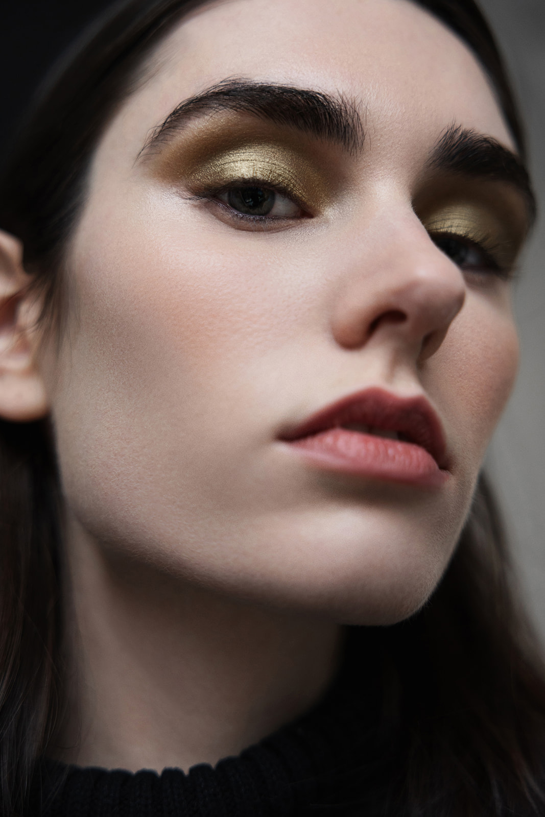 Close-up portrait of a person with dark hair, gold eye makeup, and a black high-neck top.
