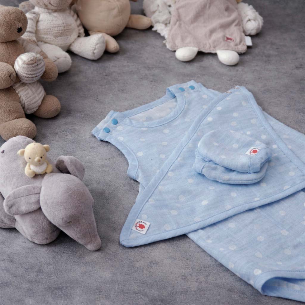 Light blue polka-dot baby garments beside several plush toys on a gray surface.