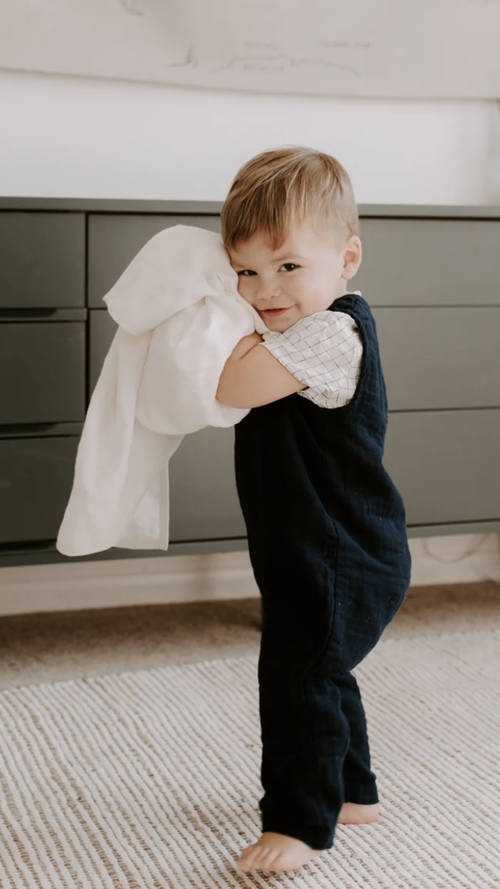 A young child hugs a white garment in front of gray cabinets.