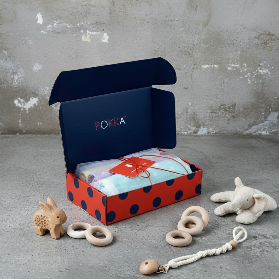 Open red-and-blue gift box with a wrapped item, beside wooden animal and ring-shaped toys on a concrete floor.