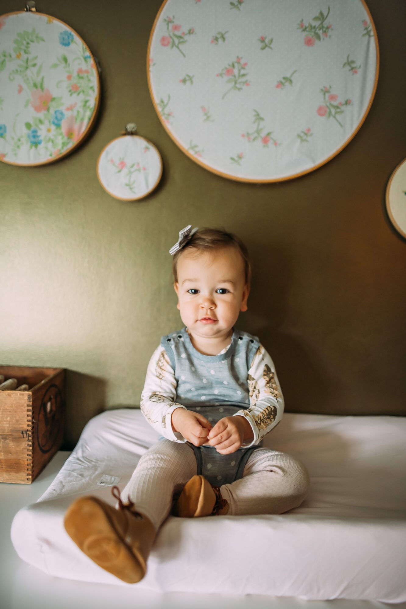 A seated child on a cushioned bench beneath several floral plates mounted on a wall.