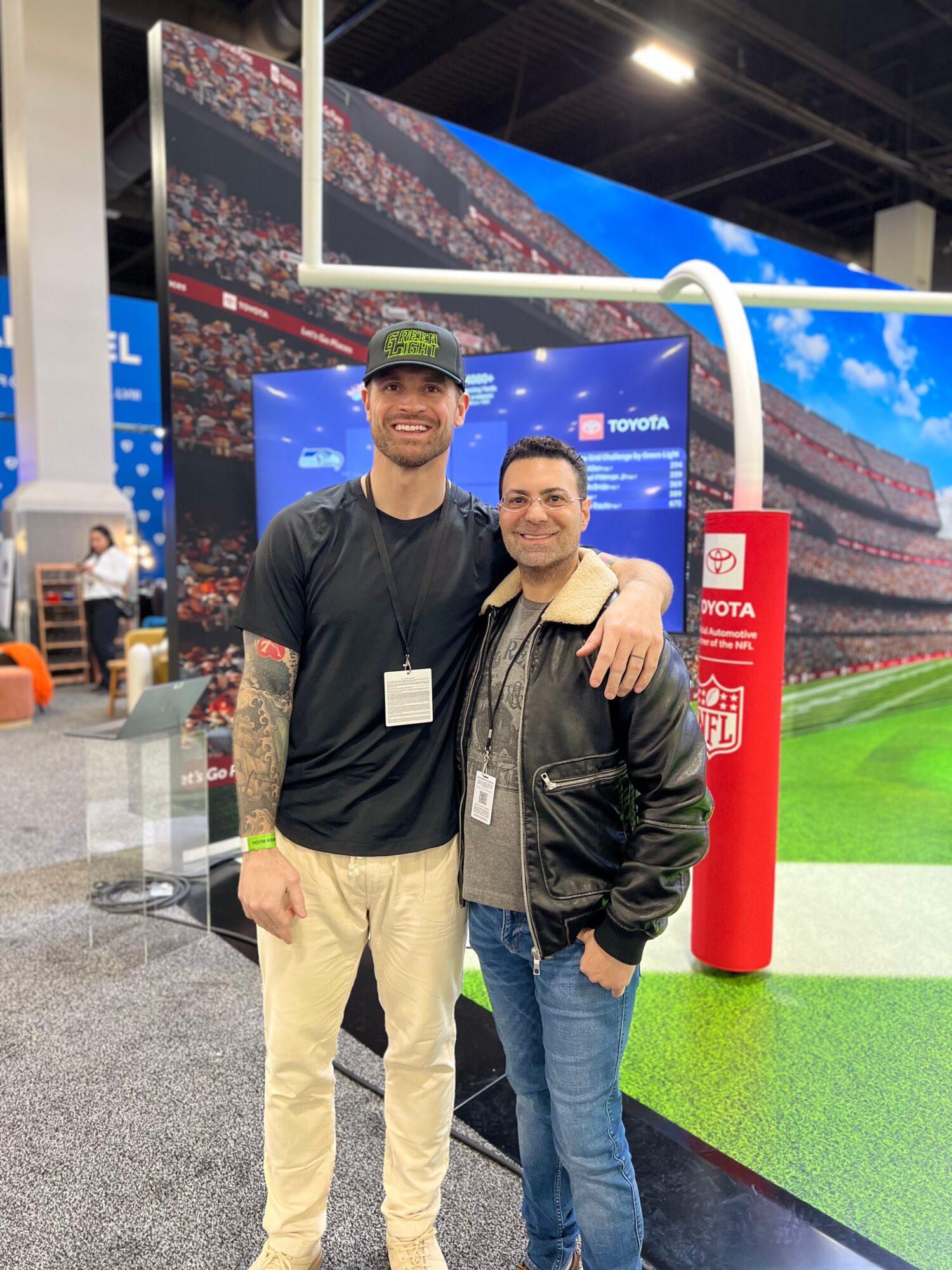 Two people stand together at a sports booth beside a red post and artificial turf.