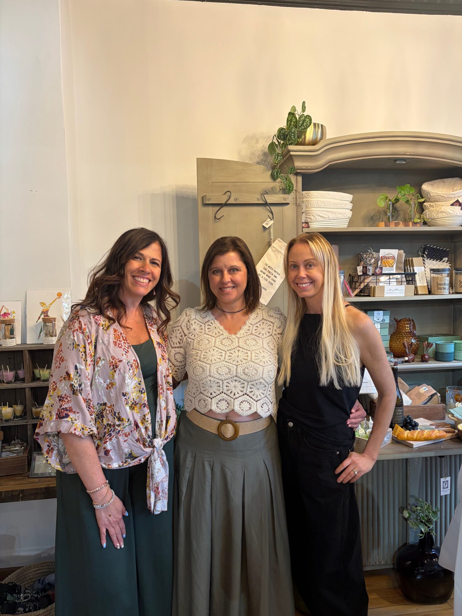 Three people stand together in a kitchen beside a counter and shelves.