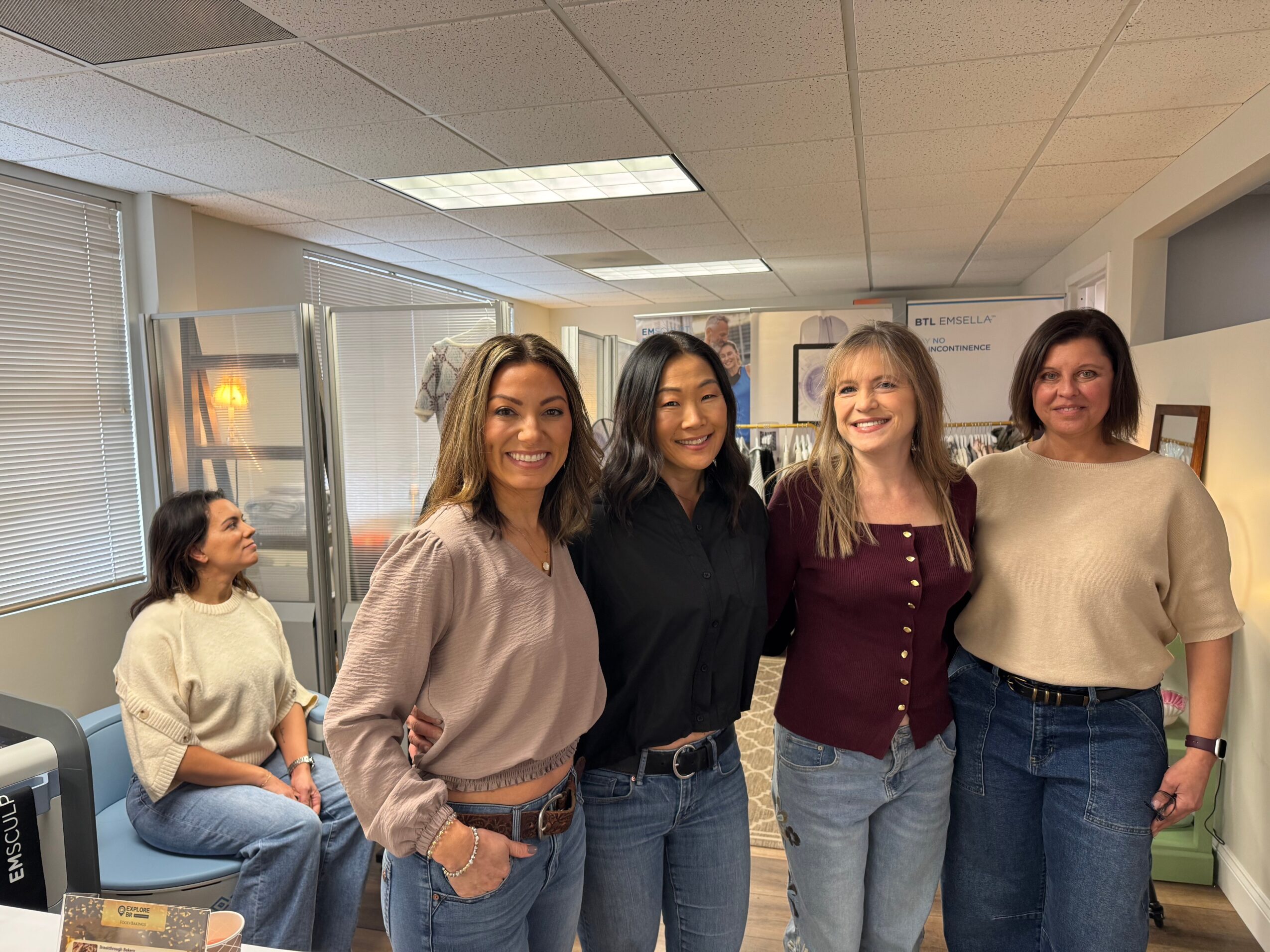 Four people stand together in an office while another person sits nearby.