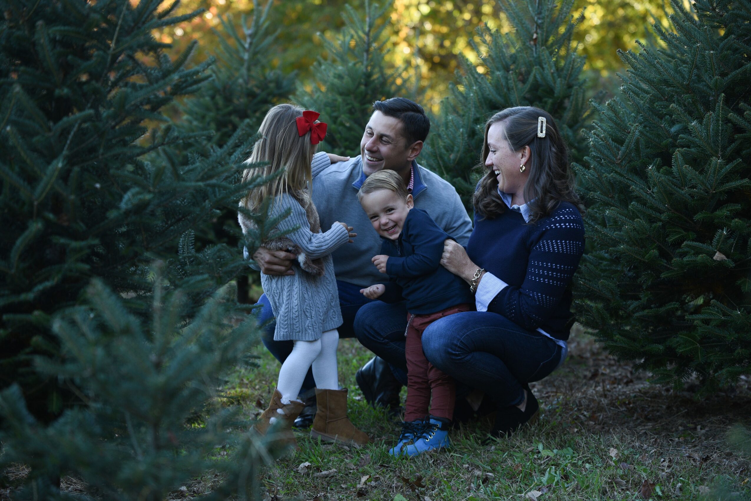 Two adults and two children pose together among evergreen trees.