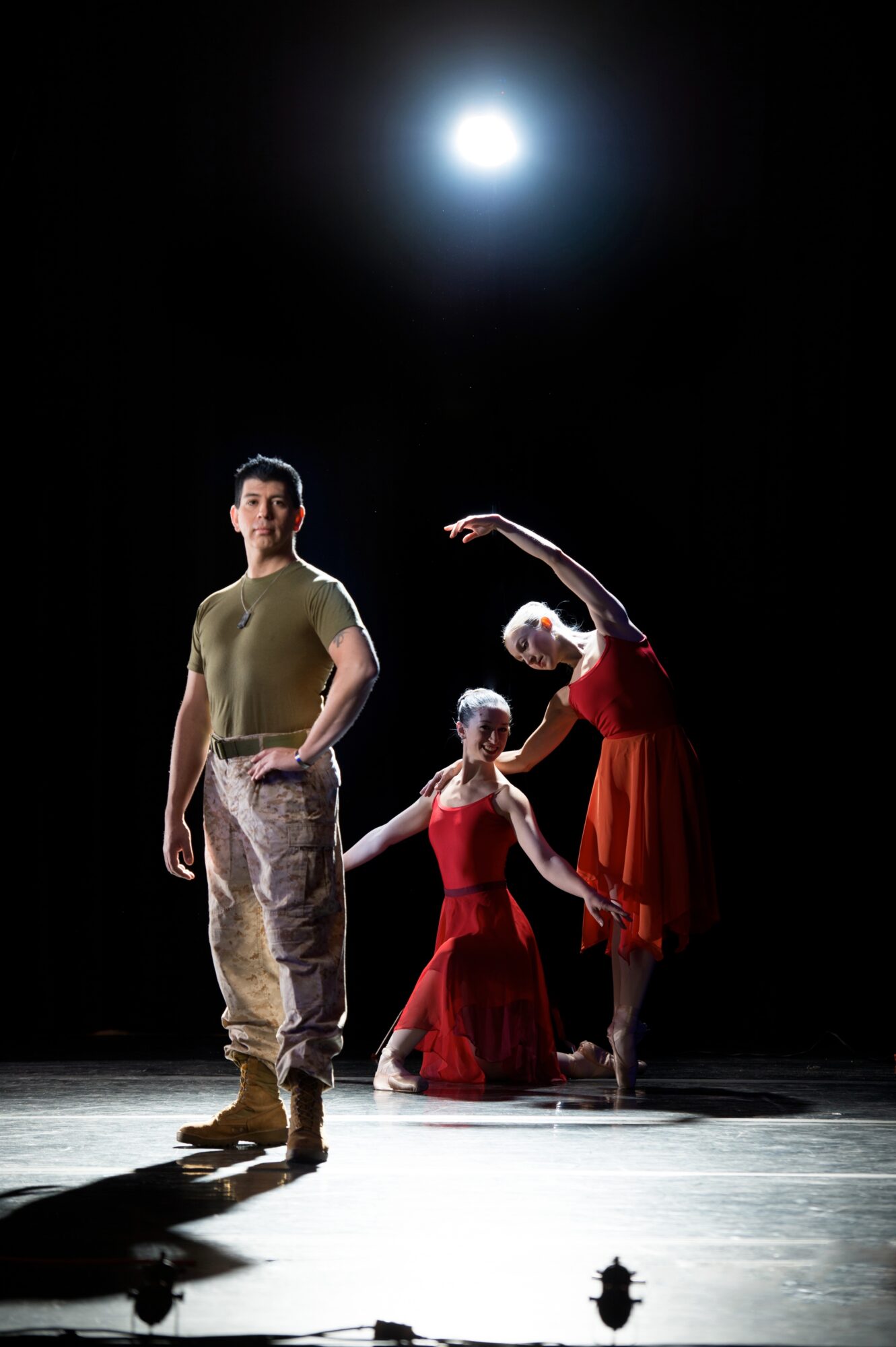 Three performers stand on a dark stage beneath a bright overhead light.