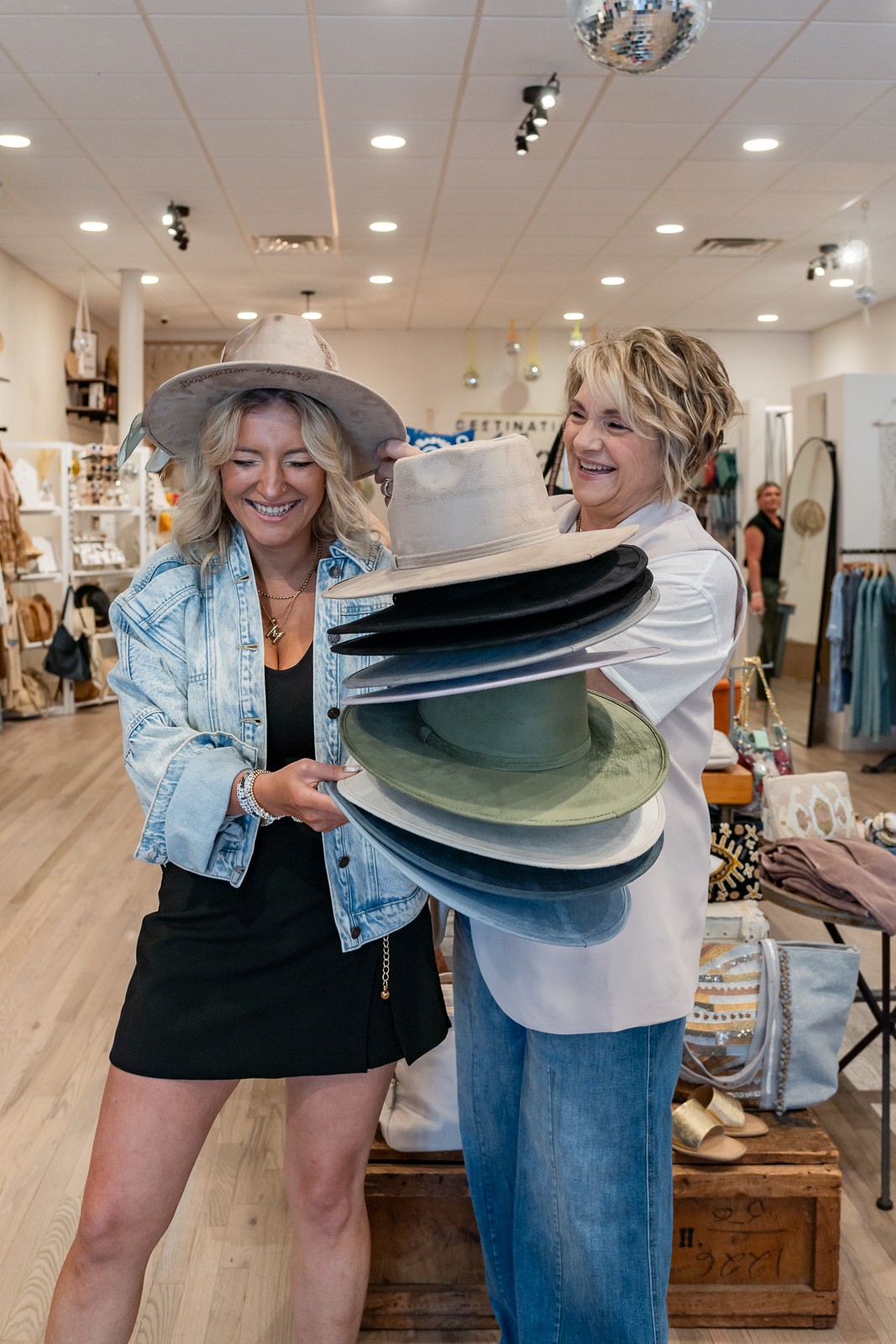 Two people hold a tall stack of wide-brimmed hats in a clothing shop.