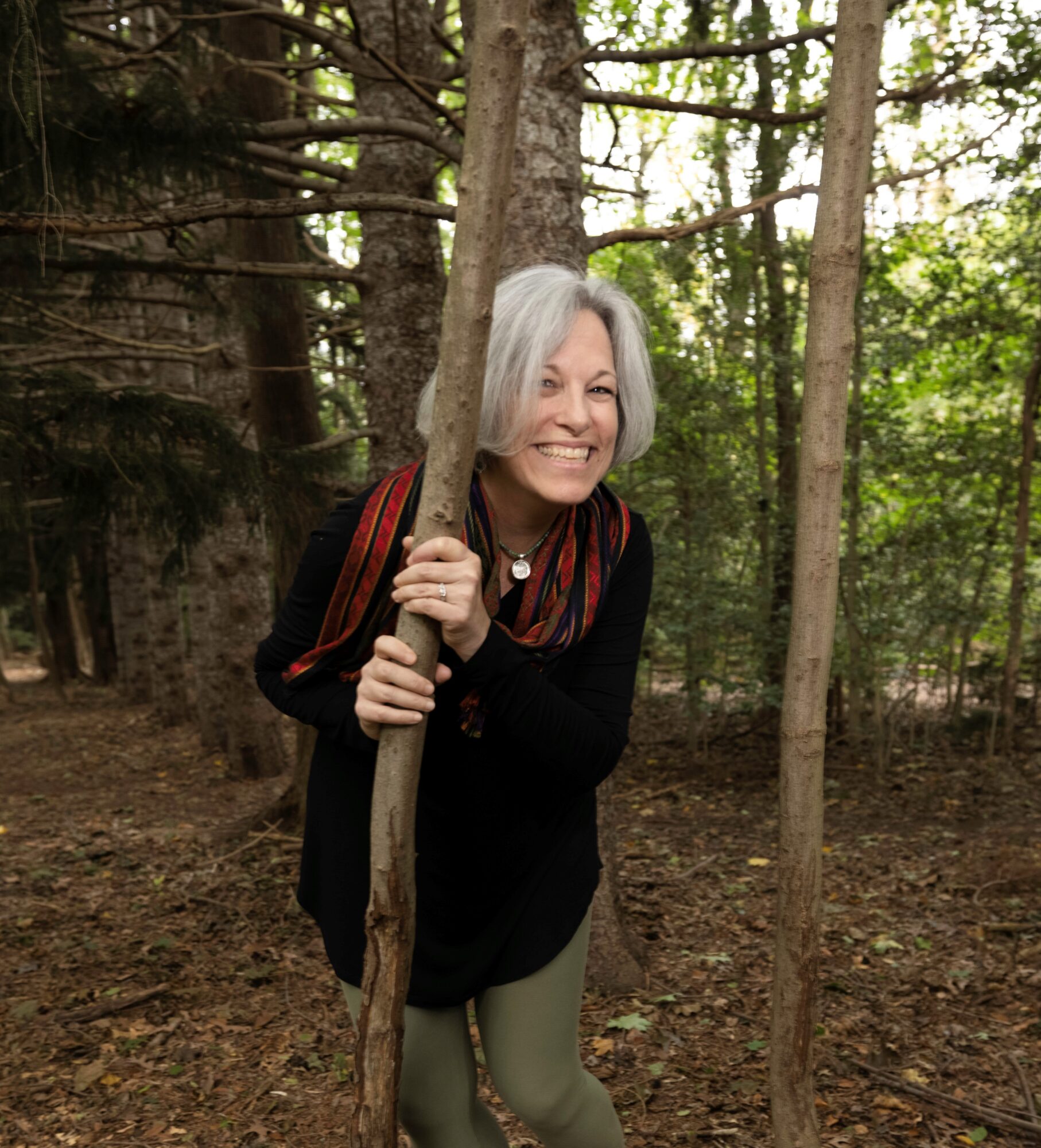 A person holding a slender tree trunk in a wooded area.