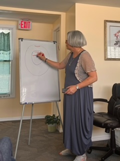 A person points to a drawing on a whiteboard beside an exit sign and a row of chairs.