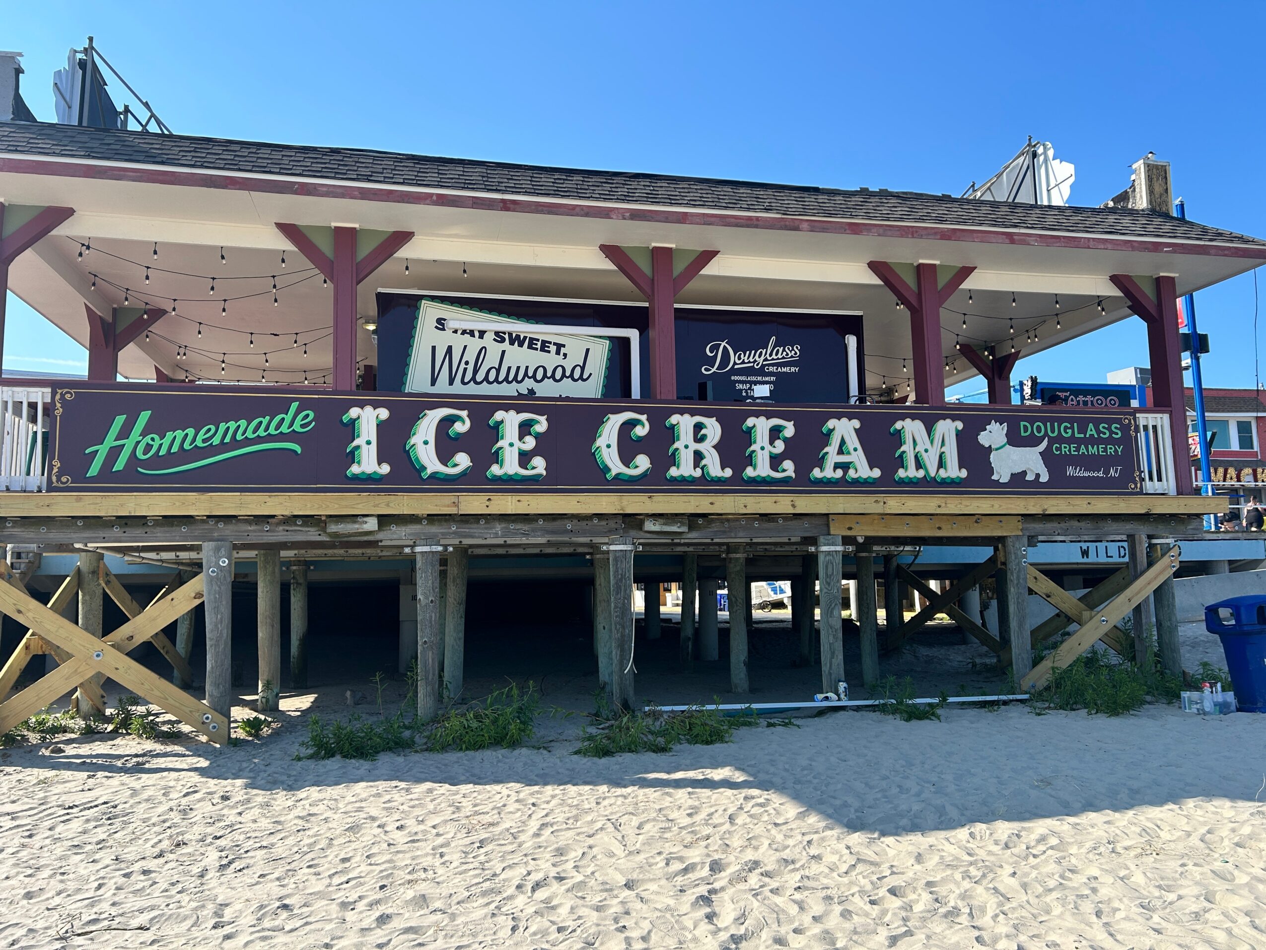 Raised beachside ice cream stand with a large green sign reading “Homemade Ice Cream” above sandy ground.