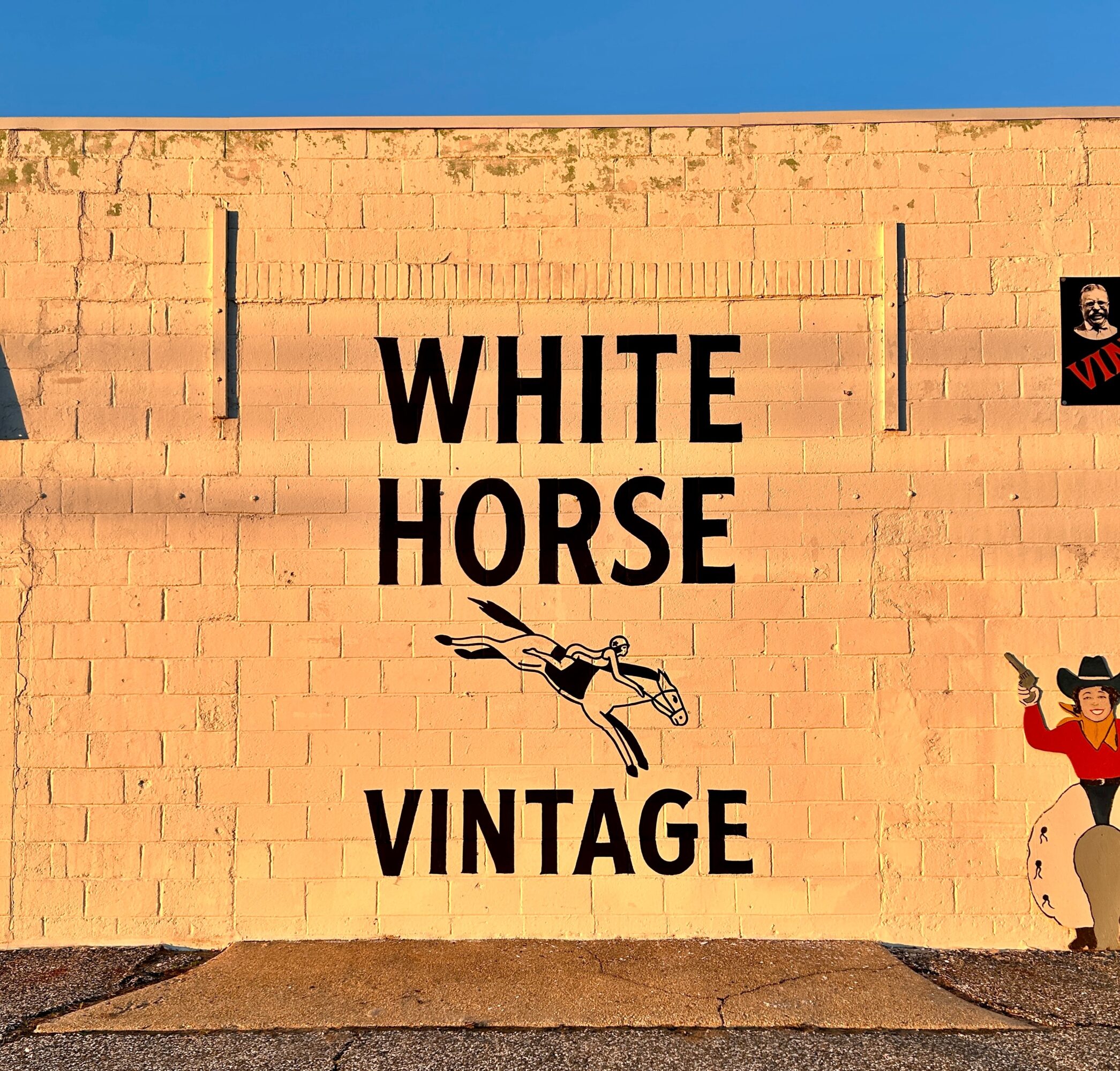 Black “WHITE HORSE VINTAGE” lettering and a jumping horse illustration on a sunlit brick wall.
