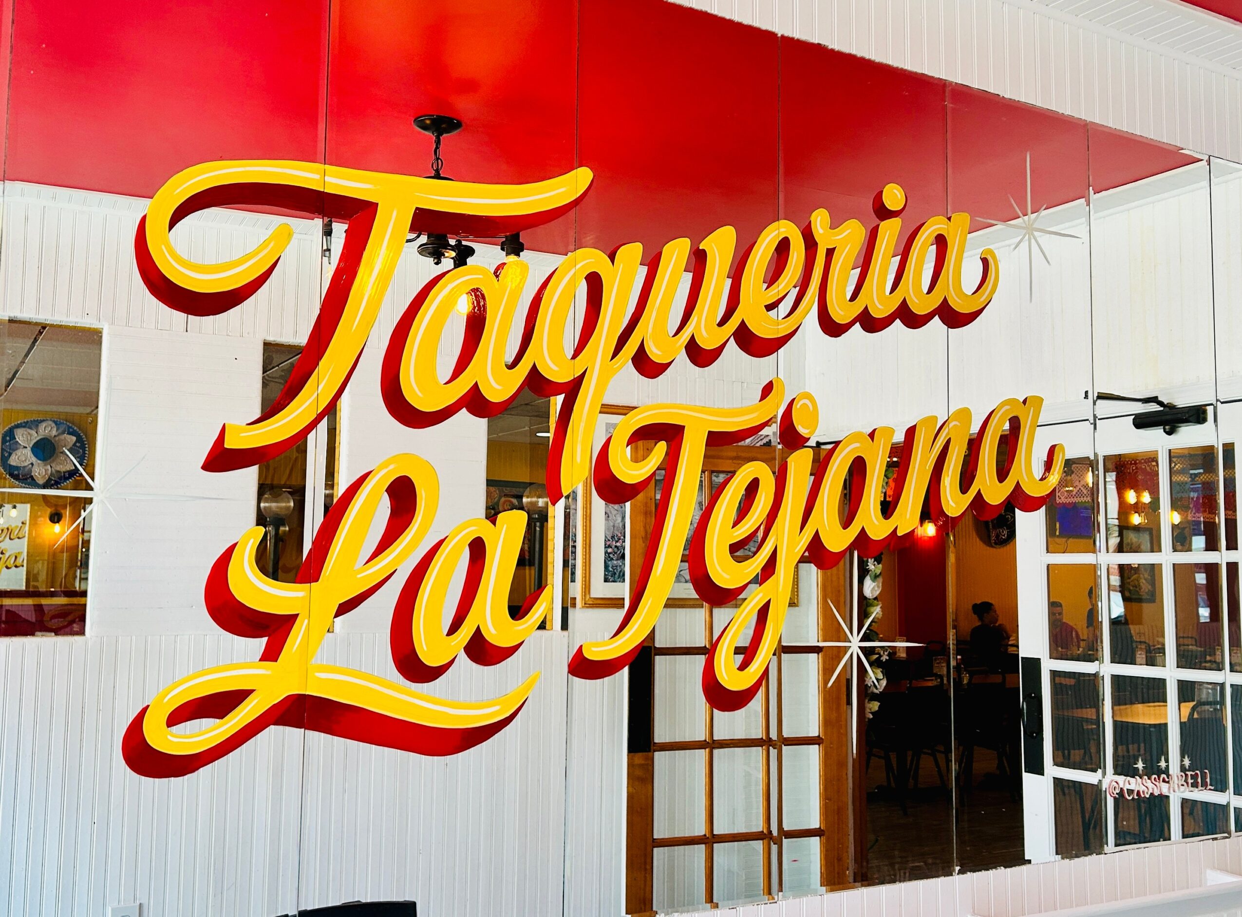 Large red and yellow “Taqueria La Tejana” sign on a red wall above restaurant windows.