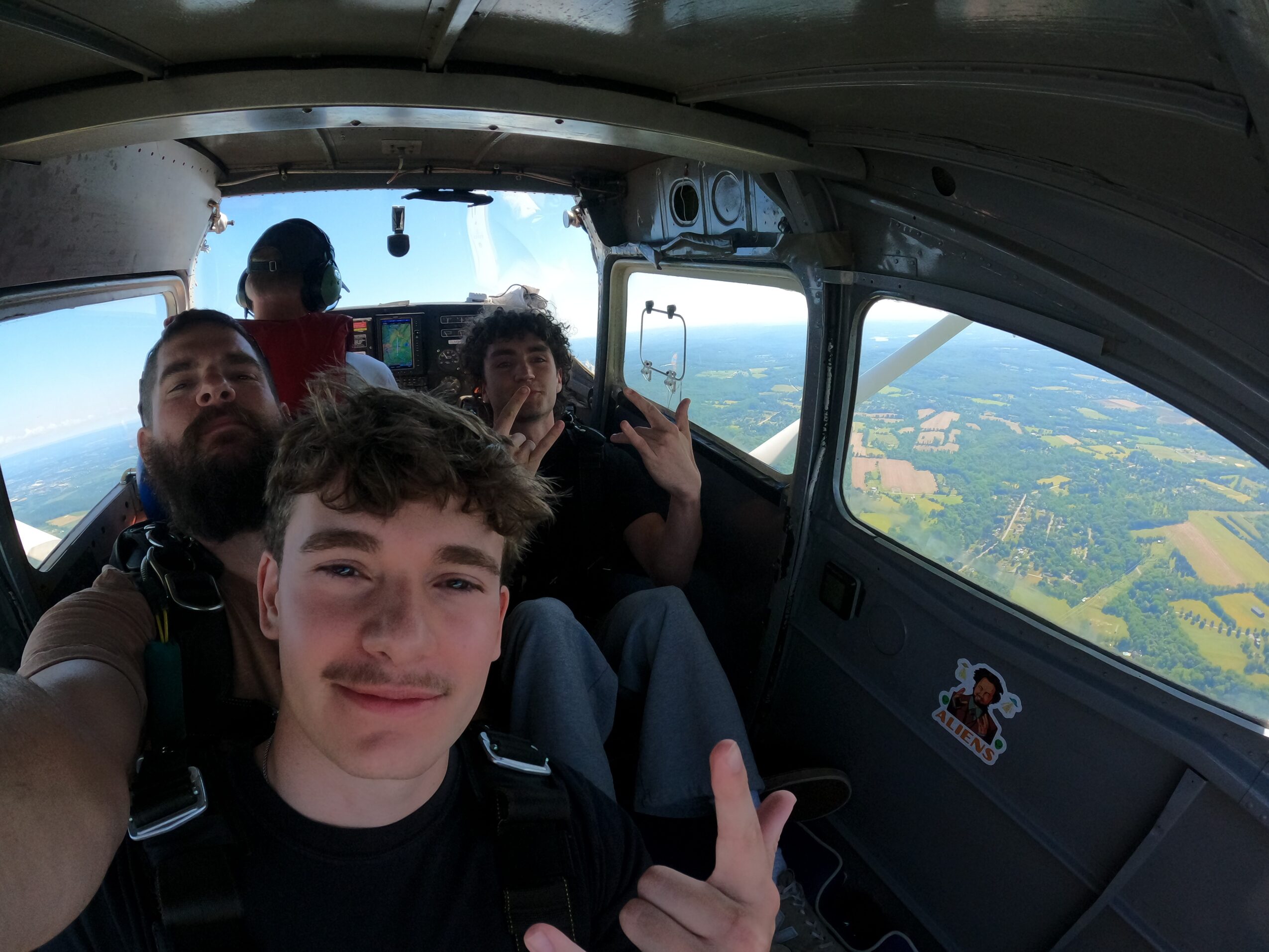 Several people pose inside a small aircraft, with farmland visible through the windows.